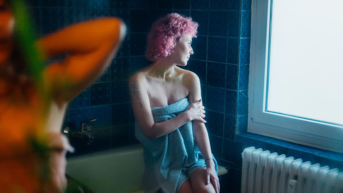 Eine junge Frau sitzt in einem Handtuch auf dem Badewannenrand (Symbolbild Körperbild)