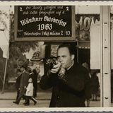 Ein Mann zielt mit einem Gewehr, im Hintergrund ein Schild