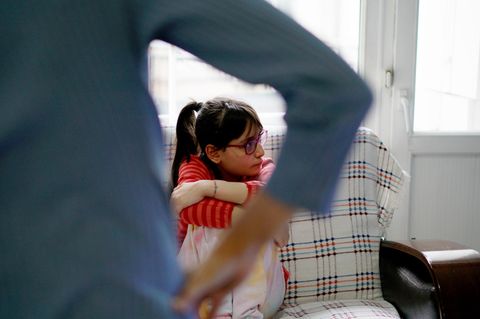 Ein Mädchen sitzt mit dem Kopf abgewandt auf einem Sofa, eine Frau steht vor ihr und wirkt wütend – Patchworkfamilie