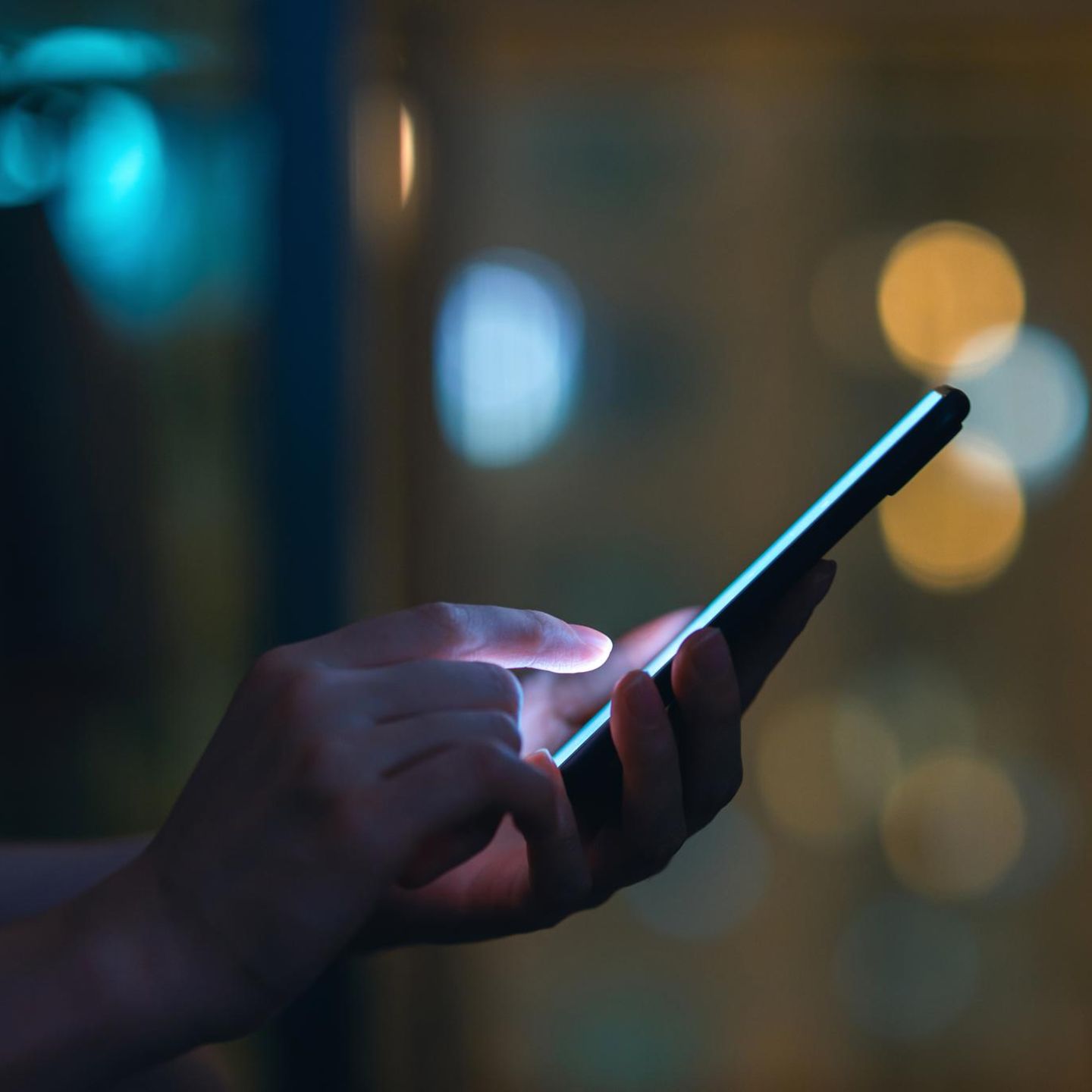 Eine Person schaut im Dunkeln auf ein leuchtendeds SMartphone und tippt SMS oder Whatsapp