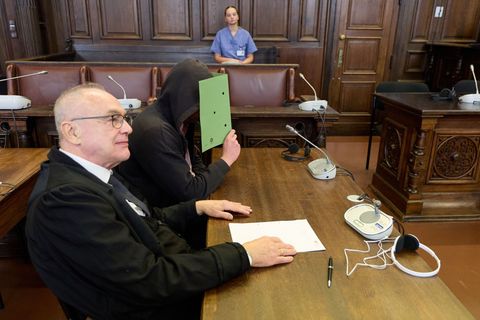 Der psychisch kranke Beschuldigte verdeckt sein Gesicht, im Hintergrund ist eine Klinikmitarbeiterin zu sehen. Foto: Georg Wendt