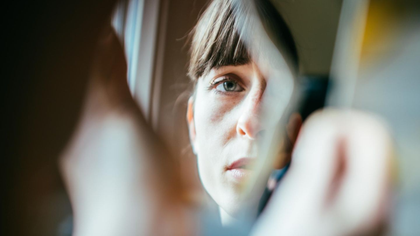 Psychisch am Limit: Frau guckt mit müden Augen in einen kaputten Spiegel