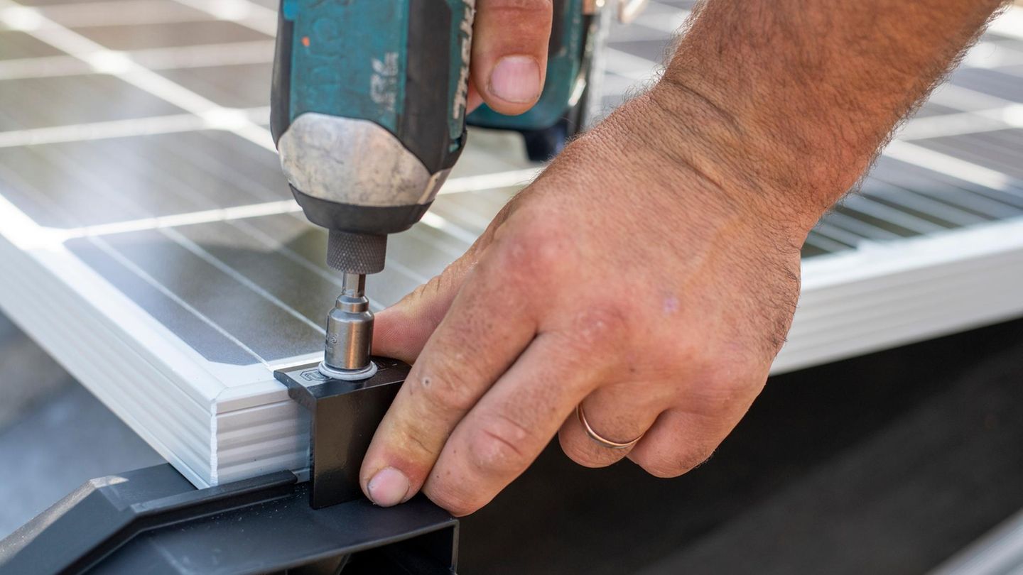 Eine Person befestigt mit einem Akkuschrauber ein Solarpanel an einem Metallrahmen, es ist nur die Hand der Person zu sehen.