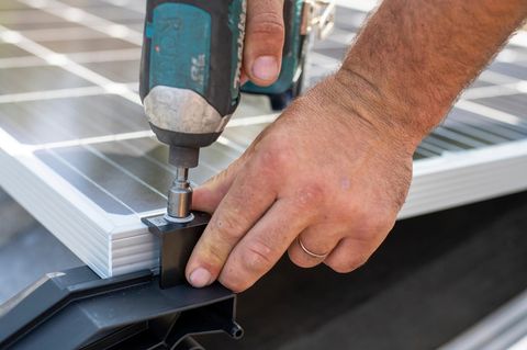 Eine Person befestigt mit einem Akkuschrauber ein Solarpanel an einem Metallrahmen, es ist nur die Hand der Person zu sehen.