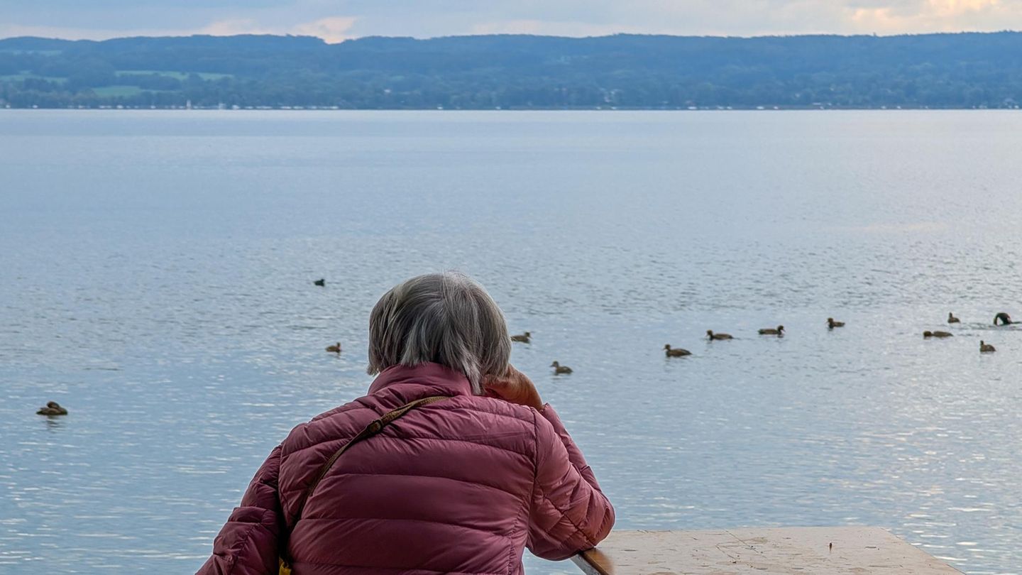 Wetter in Deutschland: Frau sitzt mit Jacke am Ammersee in Herrsching, Bayern