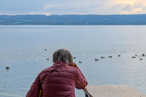 Wetter in Deutschland: Frau sitzt mit Jacke am Ammersee in Herrsching, Bayern