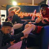 Venus 2025: Eine Darstellerin sitzt mit Sekt in der Hand auf einem Sessel und ein Mann hat ihre Stiefel im Mund