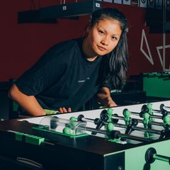 Weltmeisterin Linh Tran an einem Tischfußball leicht vorgebeugt in die Kamera blickend