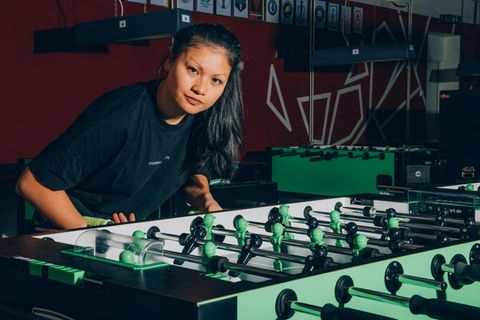 Weltmeisterin Linh Tran an einem Tischfußball leicht vorgebeugt in die Kamera blickend