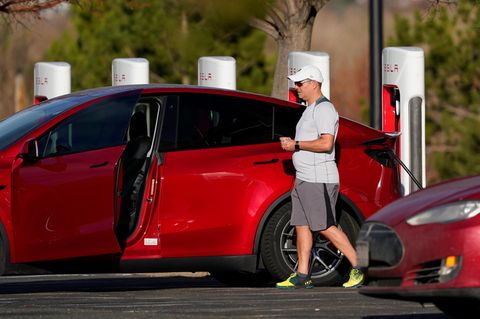 Tesla Modell Y in rot, der Fahrzeuginhaber steht daneben und lädt sein Auto auf
