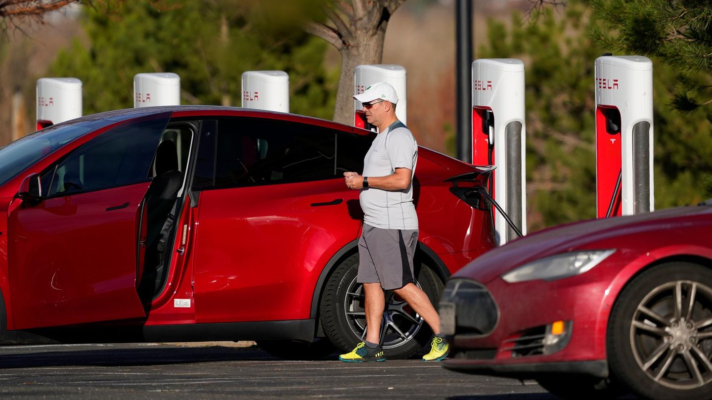 Tesla Modell Y in rot, der Fahrzeuginhaber steht daneben und lädt sein Auto auf