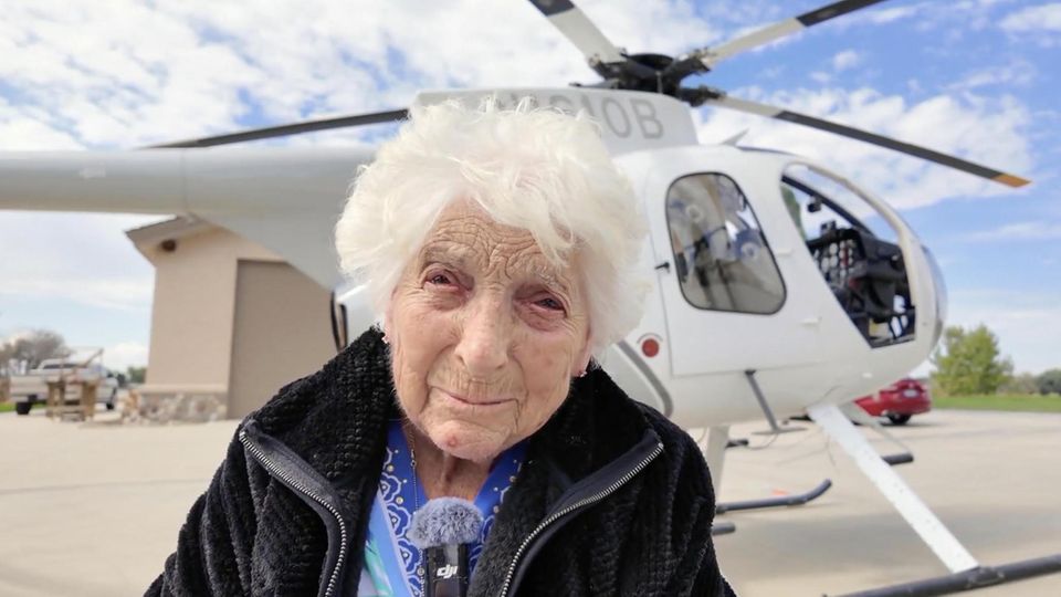 Eine alte Dame vor einem Helikopter.