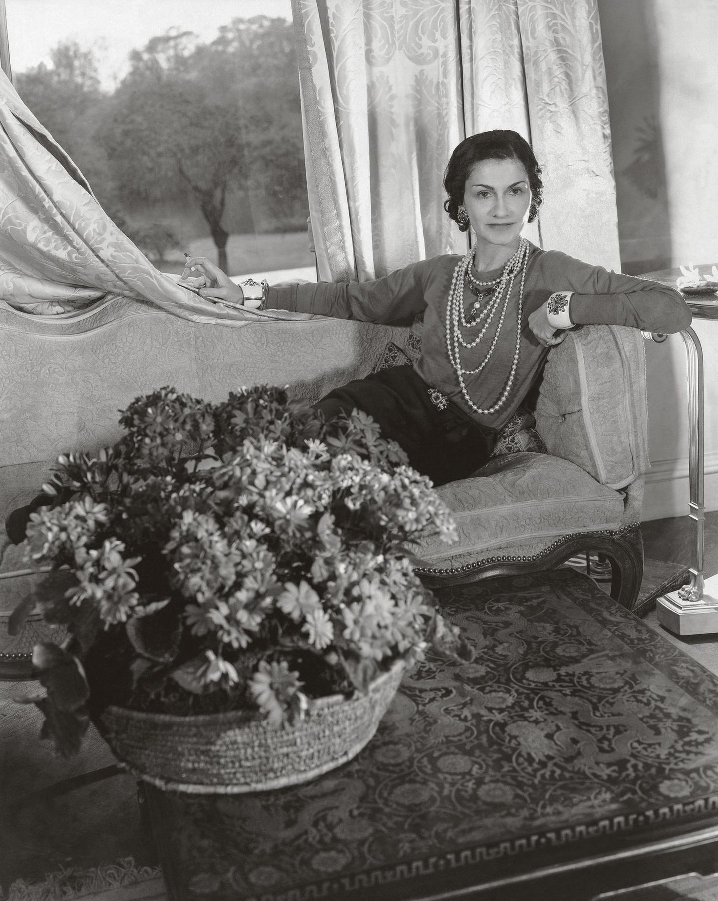 Coco Chanel in London mit einer langen, fünfreihigen Perlenkette und breiten Armreifen