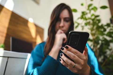 Eine junge Frau hält ein Android-Smartphone und wundert sich über den grünen Punkt