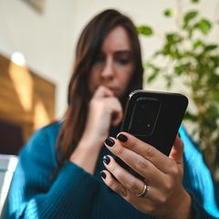 Eine junge Frau hält ein Android-Smartphone und wundert sich über den grünen Punkt