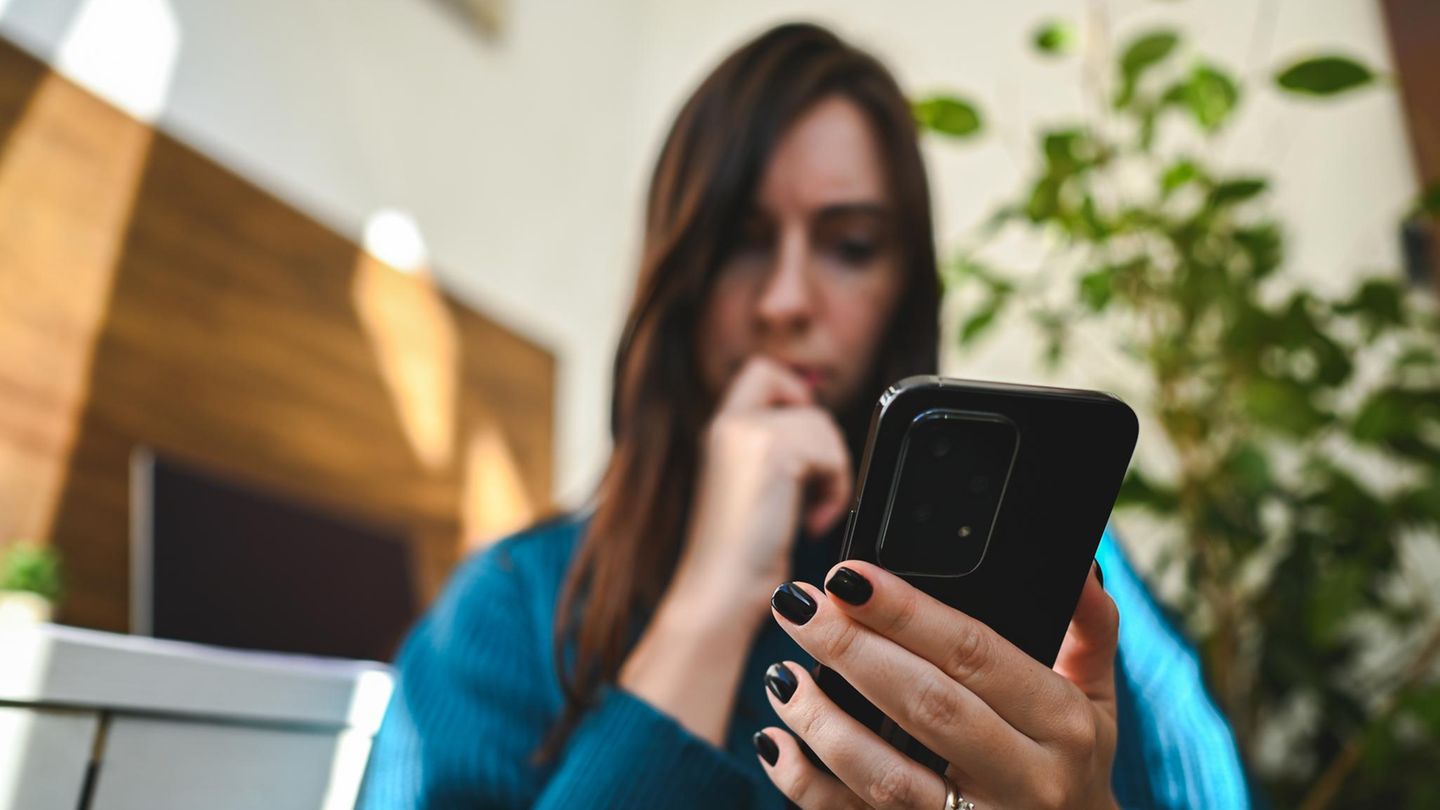 Eine junge Frau hält ein Android-Smartphone und wundert sich über den grünen Punkt