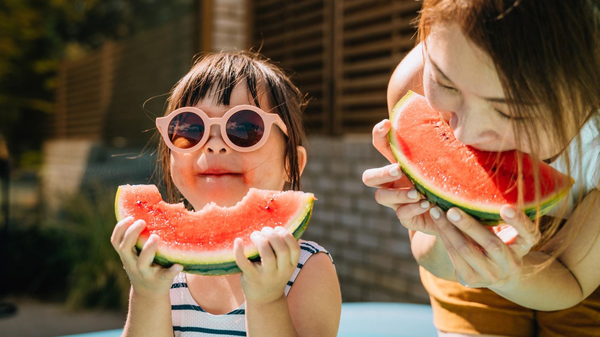 Ein kleines Kind isst mit seiner Mutter Melone. Es hat eine Sonnenbrille auf.