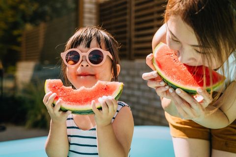 Ein kleines Kind isst mit seiner Mutter Melone. Es hat eine Sonnenbrille auf.