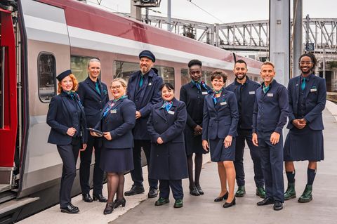 Zehn Menschen in genderneutralen Uniformen stehen neben einem Eurostar an der Gare du Nord in Paris