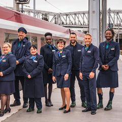 Zehn Menschen in genderneutralen Uniformen stehen neben einem Eurostar an der Gare du Nord in Paris