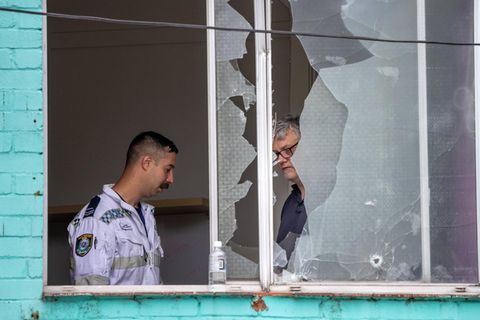 Polizisten in Sydney ermitteln am Tatort, eine zersplitterte Fensterscheibe ist zu sehen