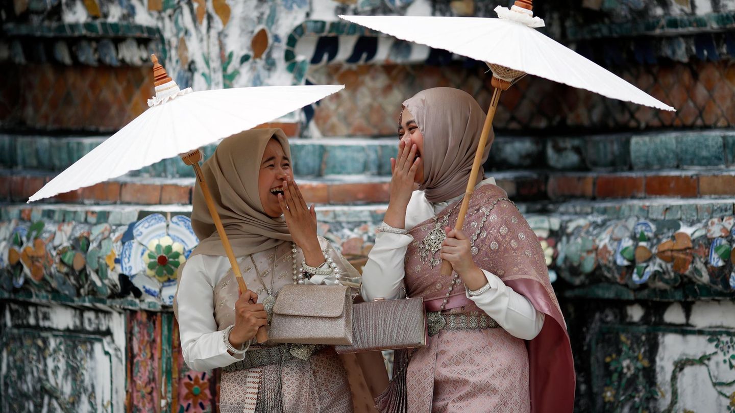 Bangkok, Thailand. Warum die Frauen kichern, ist nicht ersichtlich. Es handelt sich um muslimische Touristinnen, die in traditionellen Thai-Kleidern gewandet den prachtvollen, buddhistischen Tempel War Arun (Tempel der Morgenröte) besichtigen. Vielleicht finden sie ihr Outfit so amüsant