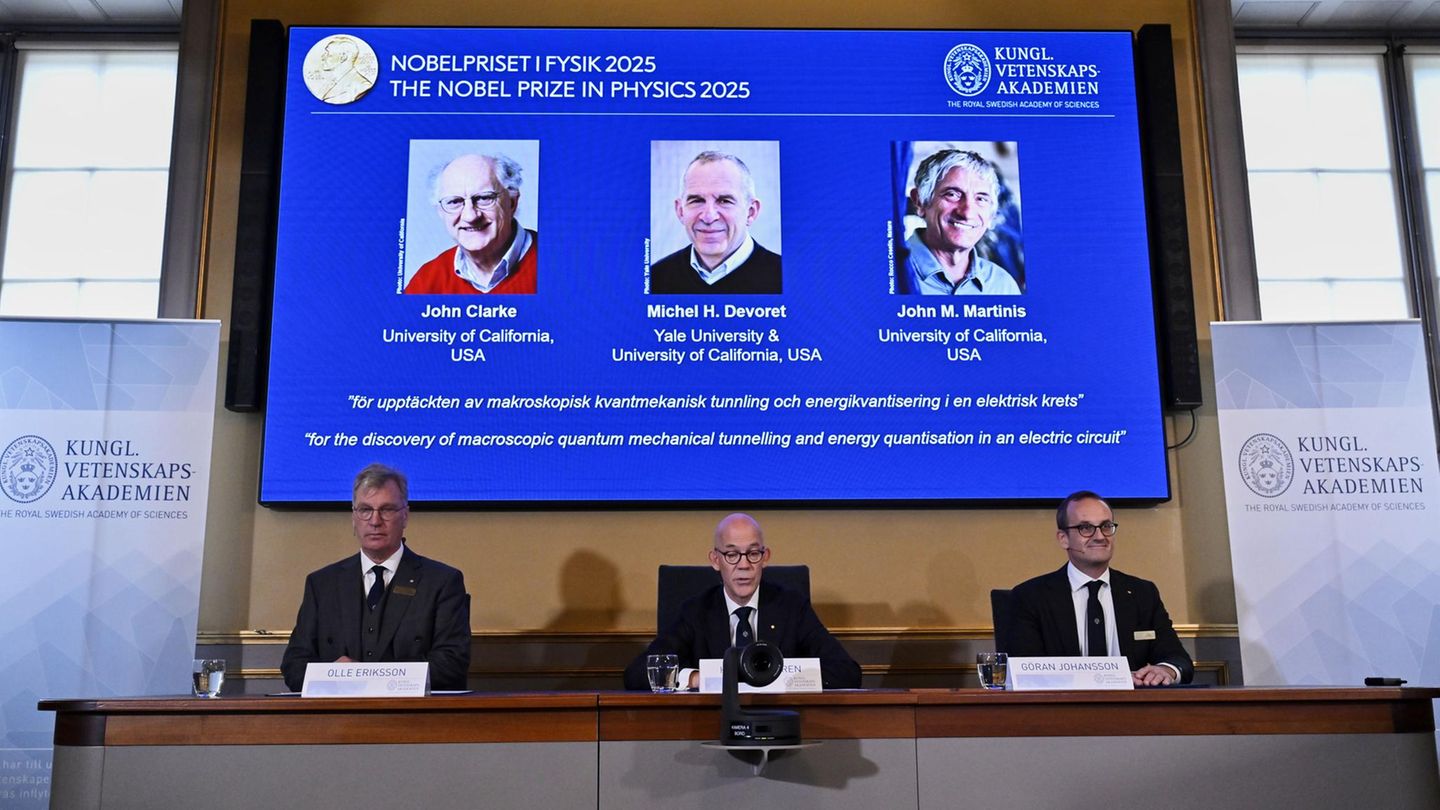 Drei weiße, ältere Männer in Anzügen verkünden die Empfänger des Nobelpreises für Physik 2025