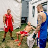 Pause in der Boxbude: Drei Kämpfer stehen und sitzen im Klappstuhl-Kreis und reden