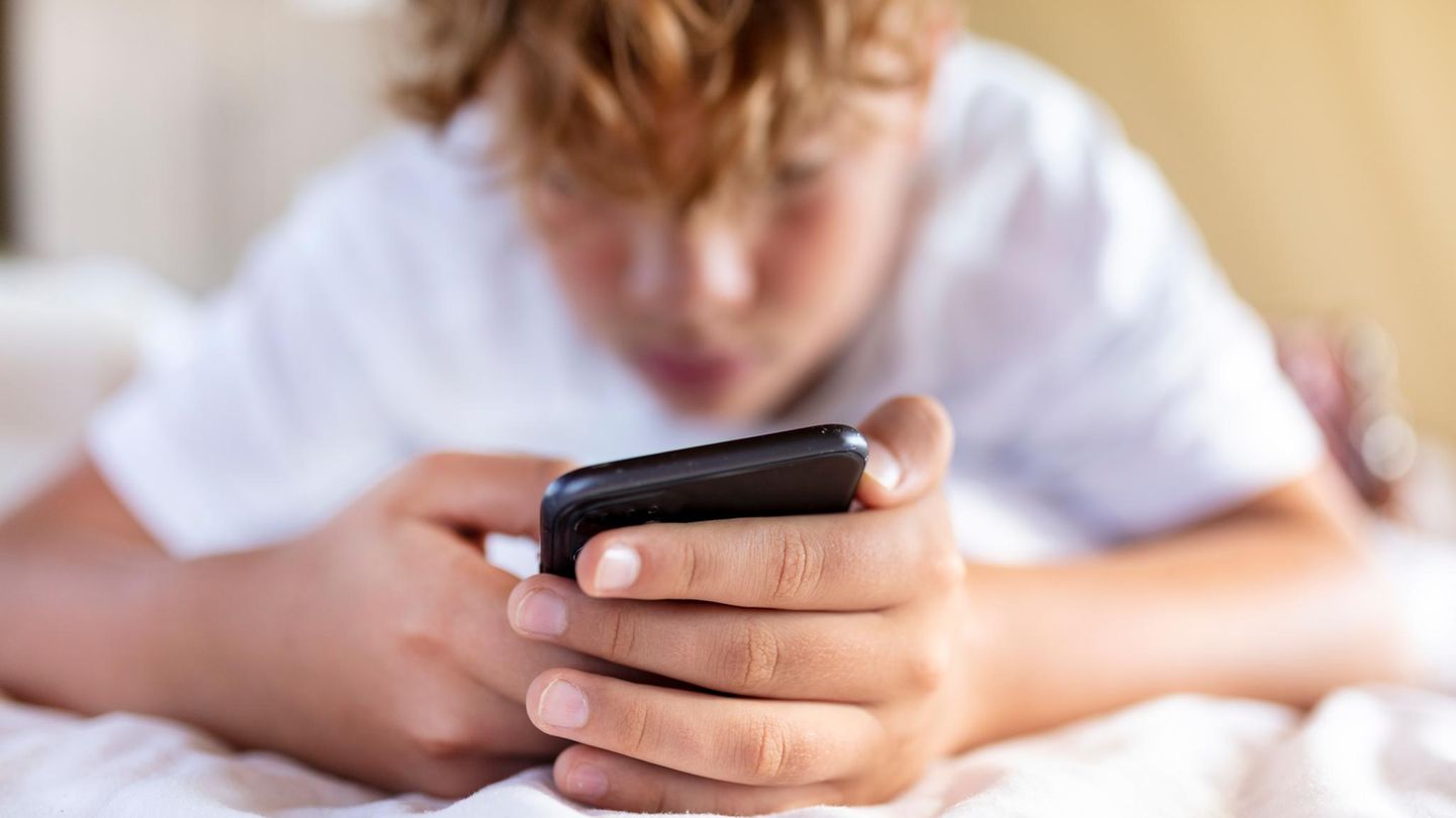 Ein Junge liegt mit Handy im Bett Ein Junge liegt mit Handy im Bett