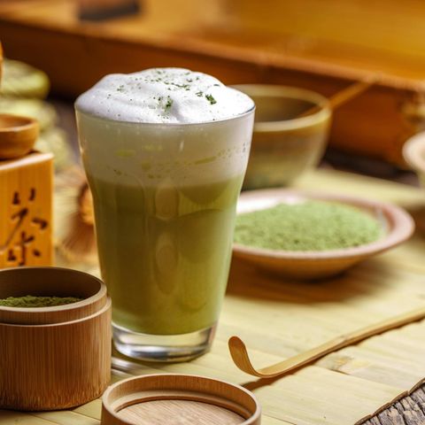 Matcha Latte im Glas auf einem Holztisch mit japanischem Geschirr