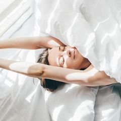 Eine Frau streckt sich alleine im Bett und lächelt (Symbolbild Singlesein)