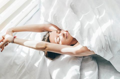 Eine Frau streckt sich alleine im Bett und lächelt (Symbolbild Singlesein)