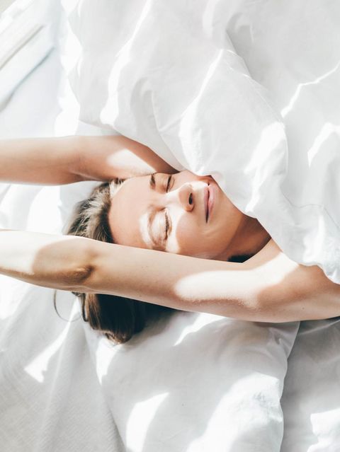 Eine Frau streckt sich alleine im Bett und lächelt (Symbolbild Singlesein)