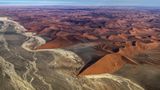 Sie wirken wie beigefarbene Wellen am roten Strand, doch es sind nur die Ablagerungen eines längst verdunstetem Flusses. Nur in besonders niederschlagsreichen Regenzeiten schafft es das Wasser aus den 150 Kilometer entfernten Naukluftbergen bis hier ins Große Sandmeer