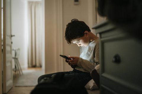 Smartphone, aber sicher: Ein Junge sitzt im Flur und starrt auf sein Handy