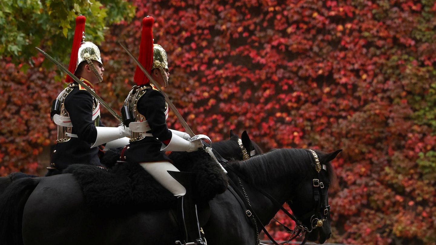 London, Großbritannien. Zwei Soldaten der berittenen Palastwache reiten an einer herbstlich-roten Hecke entlang, während der berühmte Wachwechsel vor dem House Guards stattfindet