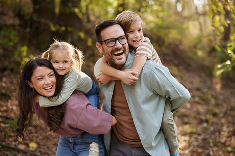 Familie Mutter Vater und zwei Kinder lachen beim Spielen draußen