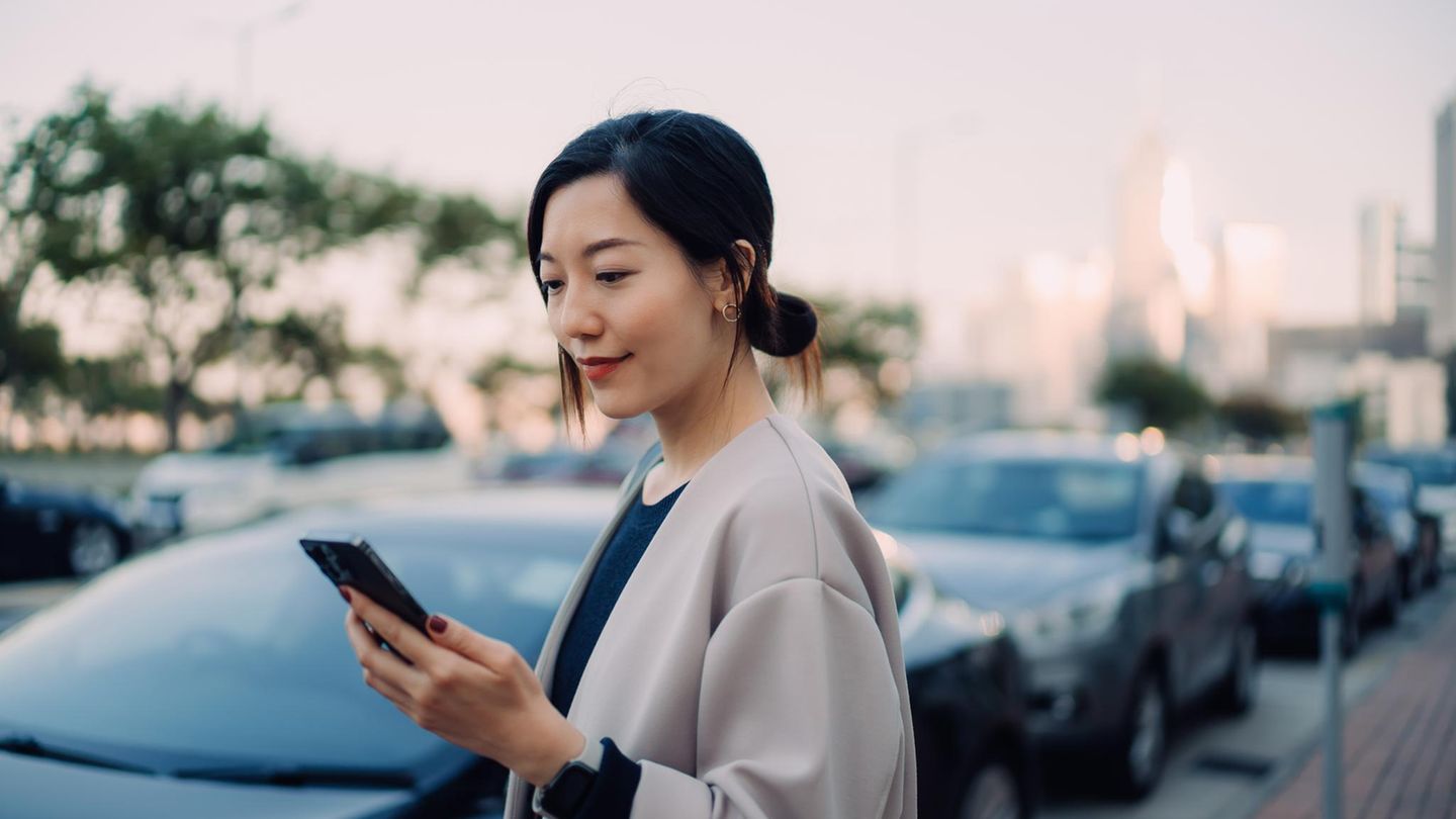Eine junge Frau schaut auf ihr Smartphone, während sie neben einem Auto steht