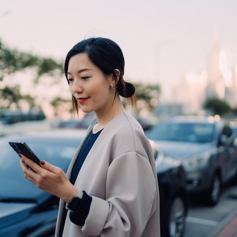 A young woman looks at her smartphone while standing next to a car