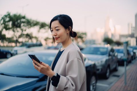 Eine junge Frau schaut auf ihr Smartphone, während sie neben einem Auto steht