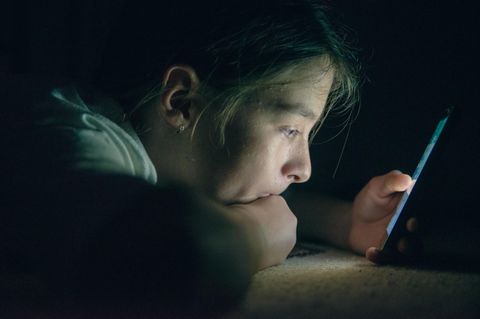 Ein Teenager starrt in einem abgedunkelten Raum auf ein Handy-Display