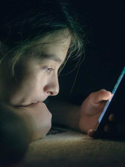 Ein Teenager starrt in einem abgedunkelten Raum auf ein Handy-Display