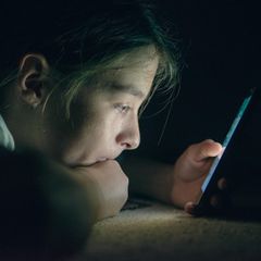 Ein Teenager starrt in einem abgedunkelten Raum auf ein Handy-Display