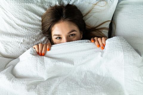 Sexcoaching: Junge Frau zieht sich Bettdecke vors Gesicht