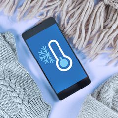 Handy vor Kälte schützen: Eine Frau macht auf einem schneebedeckten Berg ein Selfie von sich