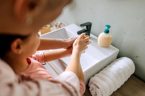 Gemeinsam Händewaschen: Eine Mutter steht hinter ihrer Tochter am Waschbecken