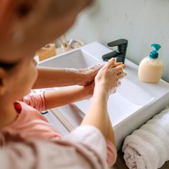 Gemeinsam Händewaschen: Eine Mutter steht hinter ihrer Tochter am Waschbecken