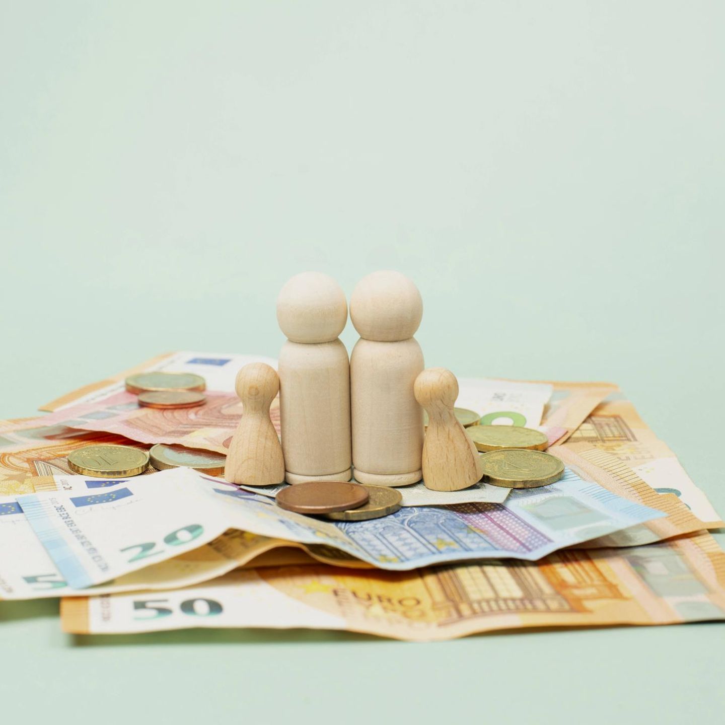 Kindergeld Symbolbild: Spielfiguren (2 große, 2 kleine) stehen auf Euroscheinen und -Münzen