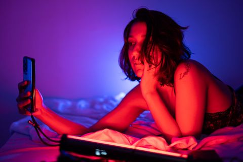 Eine Frau liegt leicht bekleidet auf dem Bett und schaut das Smartphone an. Nutzt sie ChatGPT?