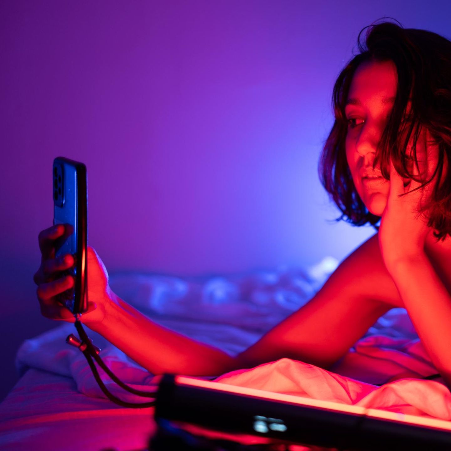 Eine Frau liegt leicht bekleidet auf dem Bett und schaut das Smartphone an. Nutzt sie ChatGPT?